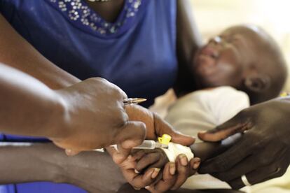 Un médico extrae una muestra de sangre a un bebé para comprobar si tiene malaria. Su cama, precisamente, no tiene mosquitera.