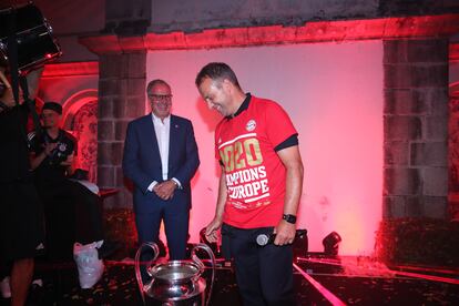 Hans Dieter Flick mira el trofeo de la Champions con Karl Heinz Rummenigge al fondo.