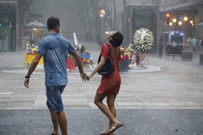 Una pareja camina bajo la lluvia el día del primer aniversario de los atentados del 17-A en Barcelona.