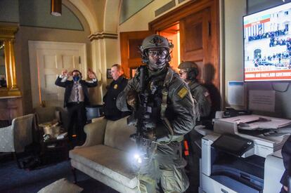 Un miembro del personal del Congreso levanta las manos mientras el equipo Swat de la policía del Capitolio revisa a todos en la sala.