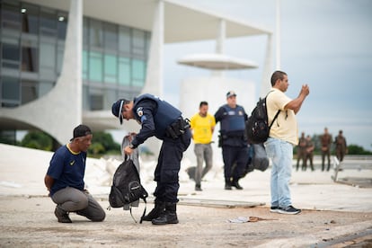 Following the invasion of the government buildings, a police officer searches the backpack of a handcuffed man.