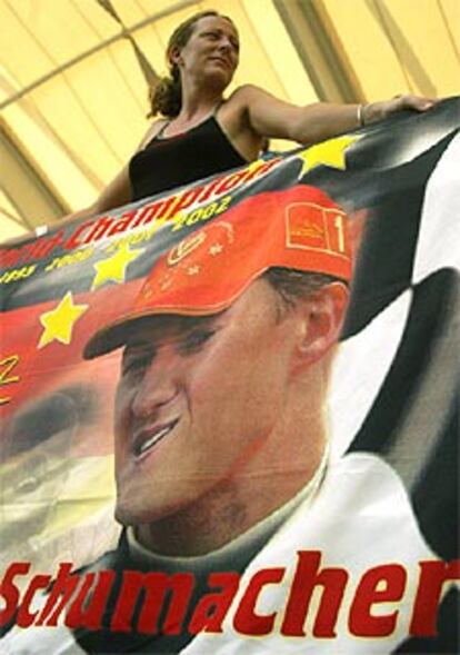 Una espectadora espera el comienzo de las carreras del Gran Premio de Malaisia junto a un cartel del piloto de Ferrari Michael Schumacher.