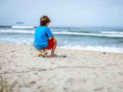 Un niño está sentado en la playa, mirando el mar.