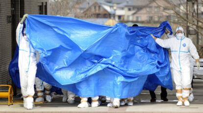 Varios operarios que trabajan en la reparación de la central de Fukushima I salen de la misma bajo una lona.