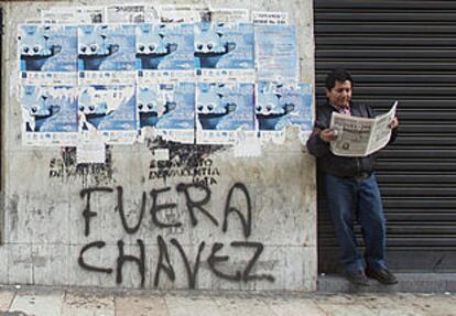 Un hombre lee un periódico ante la puerta cerrada de un comercio y junto a una pintada contra Chávez en el centro de Caracas.