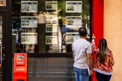 Dos personas miran los anuncios de una inmobiliaria en un barrio de Madrid.