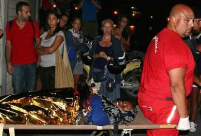 Unos turistas observan como llevan a una inmigrante en Lampedusa, Italia.