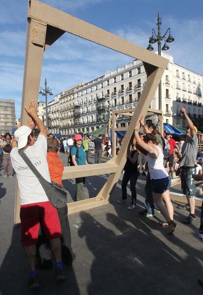 Algunos de los indignados desmontan los armazones que han servido de estructura de su campamento y los fotógrafos, cuya sombra se proyecta en el suelo, intentan retratar el marco con la renovada imagen de la plaza.