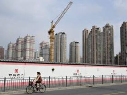 En la imagen, una mujer pasa con su bicicleta frente a una construcción en Shanghái (China). EFE/Archivo