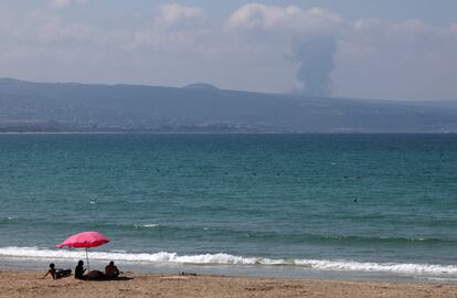 Varias personas observan desde una playa de Tiro (Líbano) una columna de humo elevándose tras el ataque israelí.
