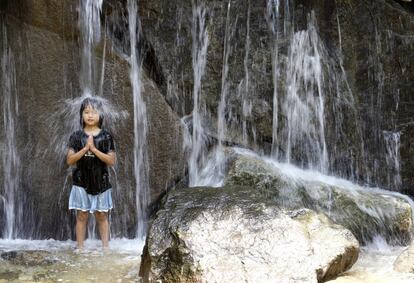 Una niña, bajo una cascada en la posición de meditación de los monjes budistas mientras juega en el Parque Asuka en Tokio.