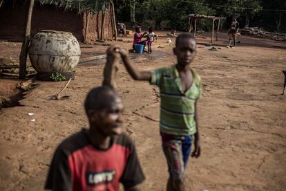 Moise, de 10 años, y su abuelo se preparan antes del trabajo en los campos de cacao mientras una vecina baña a su hija en el campamento de Bodouakro.