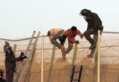 Un agente junto a dos inmigrantes en la valla.