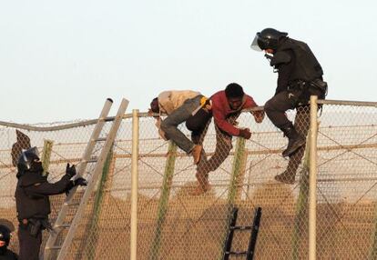 Un agente junto a dos inmigrantes en la valla. 