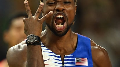 Noah Lyles, sin cadena al cuello, muestra tres dedos, por sus tres oros, tras ganar el relevo.