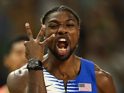 Noah Lyles, sin cadena al cuello, muestra tres dedos, por sus tres oros, tras ganar el relevo.