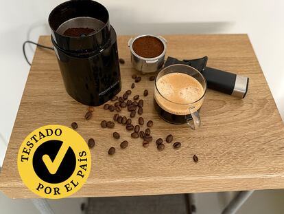 Un molinillo con gramos de café y una taza encima de una mesa.