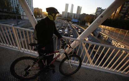 Un ciclista contempla el tráfico por la carretera de Colmenar y el cartel informativo en la avenida de la Ilustración.