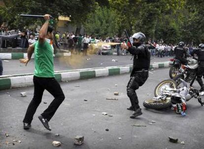 Un agente antidisturbios iraní arroja gas lacrimógeno sobre un partidario de Musaví que le ataca con una porra policial.