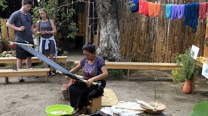 Dos turistas observan a una mujer indígena mientras teje en San Juan La Laguna, una comunidad en la cuenca del Lago Atitlán.