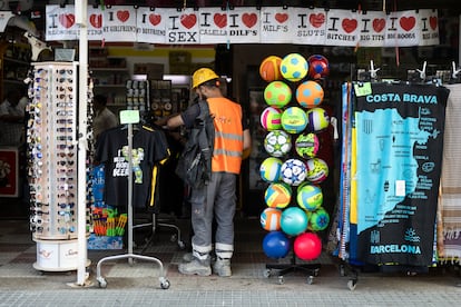 Un trabajador brasileño mira camisetas en una tienda de souvenirs frente al hotel en el que se aloja, en Calella.