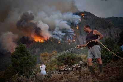 Vecinos de la localidad de Aguamansa intentaban refrescar los alrededores de sus viviendas ante la amenaza de incendio descontrolado, el jueves.