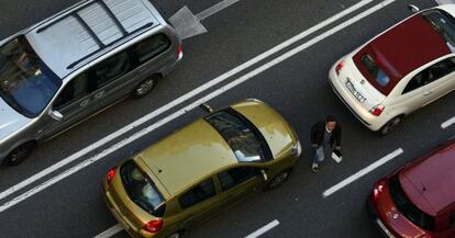 Un peat&oacute;n cruza la calzada entre coches en la Gran V&iacute;a de Madrid.