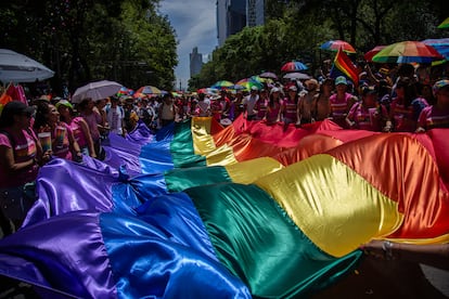 Asistentes a la marcha sostienen una bandera con los colores del arcoíris.