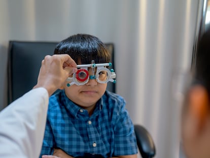 Las manos del personal óptico tocan y sostienen las herramientas oculares que usa un niño pequeño para revisar los ojos.