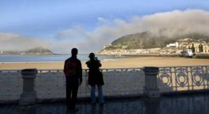 En la imagen, una pareja de turistas toman una fotografía desde la playa de la Concha de San Sebastián. EFE/Archivo