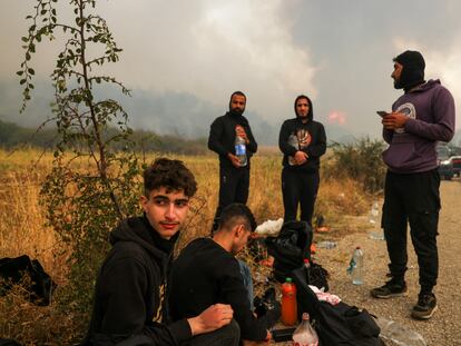 Un grupo de migrantes encontrado por los bomberos griegos permanece al lado de una carretera, mientras sigue activo el incendio en el parque nacional de Dadiá, en la región de Evros (Grecia), este viernes.