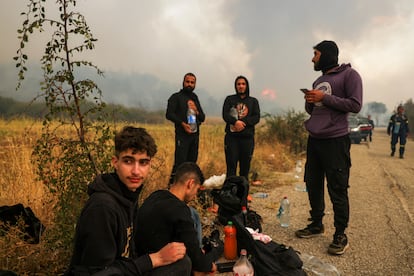 Un grupo de migrantes encontrado por los bomberos griegos permanece al lado de una carretera, mientras sigue activo el incendio en el parque nacional de Dadiá, en la región de Evros (Grecia), este viernes.