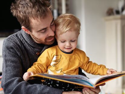 Cropped shot of an adorable little boy reading a book while sitting with his father at home