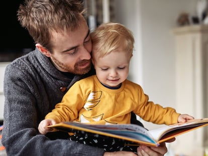 Cropped shot of an adorable little boy reading a book while sitting with his father at home