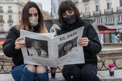 Dos jóvenes leen EL PAÍS en un banco en Madrid.