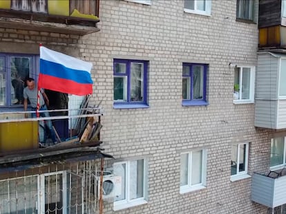 Un hombre coloca una bandera nacional rusa en un balcón de un edificio residencial en Lisichansk, en una imagen distribuida por el Ministerios de Defensa ruso.