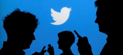 People holding mobile phones are silhouetted against a backdrop projected with the Twitter logo  in Warsaw