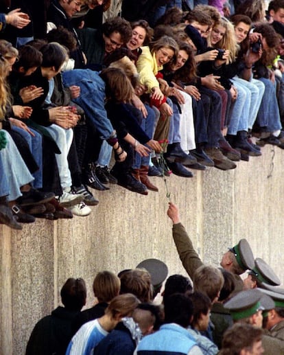 Un agente de la policía de la Alemania del Este ofrece un clavel rojo a un grupo de berlineses sentados en el alto del muro de Berlín, cerca de la puerta de Brandenburgo.