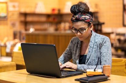 Una joven trabaja en una cafetería con su ordenador portátil y un teléfono móvil.