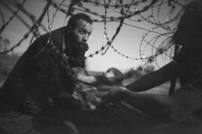 Esta imagen del fotógrafo australiano Warren Richardson ha sido la ganadora de la 59 edición de la fotografía del año World Press Photo, la máxima distinción del fotoperiodismo mundial. La fotografía, en blanco y negro, muestra un hombre pasando a un bebe a través de la valla de alambre de espino en Roeszke, en la frontera entre Serbia y Hungría, el 28 de agosto de 2015. "Yo estaba en el lado serbio, donde casi no había policía, apenas un coche y no estaban haciendo nada. Los refugiados podían tener problemas en el lado húngaro si se encontraban con los guardias fronterizos", ha explicado Richardson. La foto, continúa, está tomada de noche y sin flash, porque si la hubiera hecho con flash la policía habría venido. Richardson mandó la imagen a varias agencias de noticias, pero ese verano ninguna quiso comprársela. "La subí a la red social Facebook y unas 29 personas le dieron al botón "me gusta", eso es todo", ha concluido, mientras se encogía de hombros.