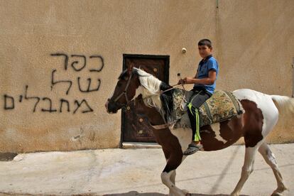 Un niño palestino monta a caballo frente a una inscripción que dice en hebreo "aldea de terroristas", en la aldea de Deir Estya.