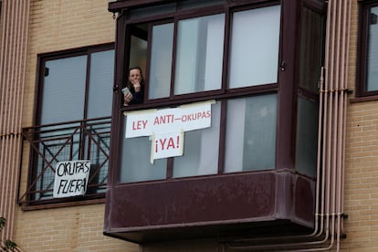 Una mujer mira desde la ventana de su apartamento con carteles de apoyo a los desalojos.
