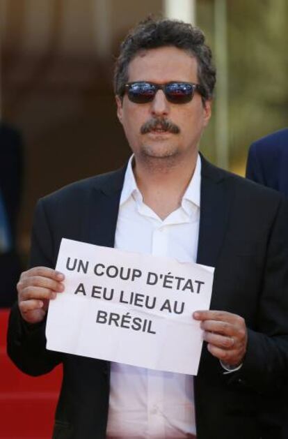 No tapete vermelho de Cannes, Kleber Mendonça Filho segura cartaz no qual denuncia que “um golpe de Estado aconteceu no Brasil”.