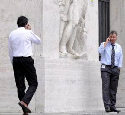 Dos consultores financieros hablan por teléfono móvil junto al edificio de la Bolsa en la plaza Affari de Milán (Italia). EFE/Archivo