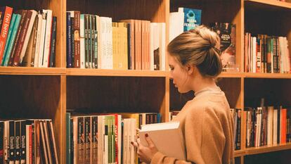 Una estudiante universitaria examina libros frente a las estanterías de una biblioteca