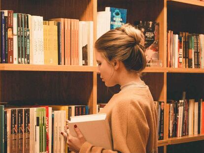 Una estudiante universitaria examina libros frente a las estanterías de una biblioteca