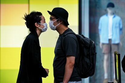 Una pareja con máscaras se acerca para besarse mientras hacen fila para realizarse test de covid en Pekín, este lunes.