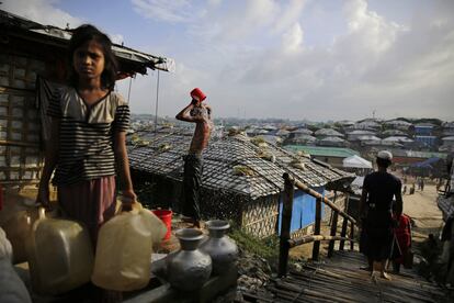 Un refugiado rohingya se lava mientras una niña rellena garrafas de agua en el campo de refugiados de Kutupalong (Bangladés), el 22 de agosto de 2018.