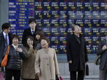 Viandantes caminan frente a una pantalla que muestra los indicadores de las principales bolsas mundiales, en Tokio, Japón. EFE/Archivo