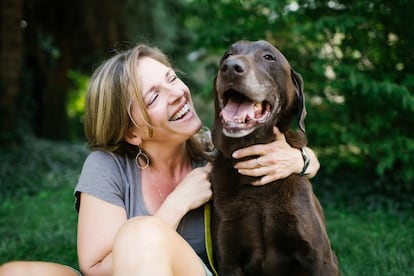 Smiling woman sitting on the grass with a Labrador Retriever.